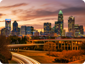 Charlotte city skyline at twilight with light trails on a highway in the foreground.