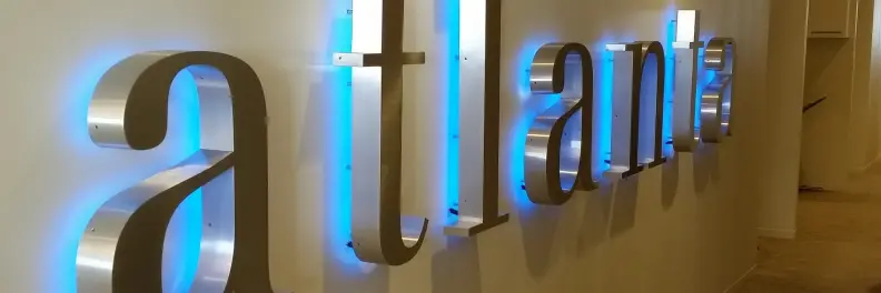 Metallic sign spelling "atlanta" with blue backlighting on a wall.