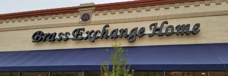 Storefront with "Brass Exchange Home" sign and blue awning.